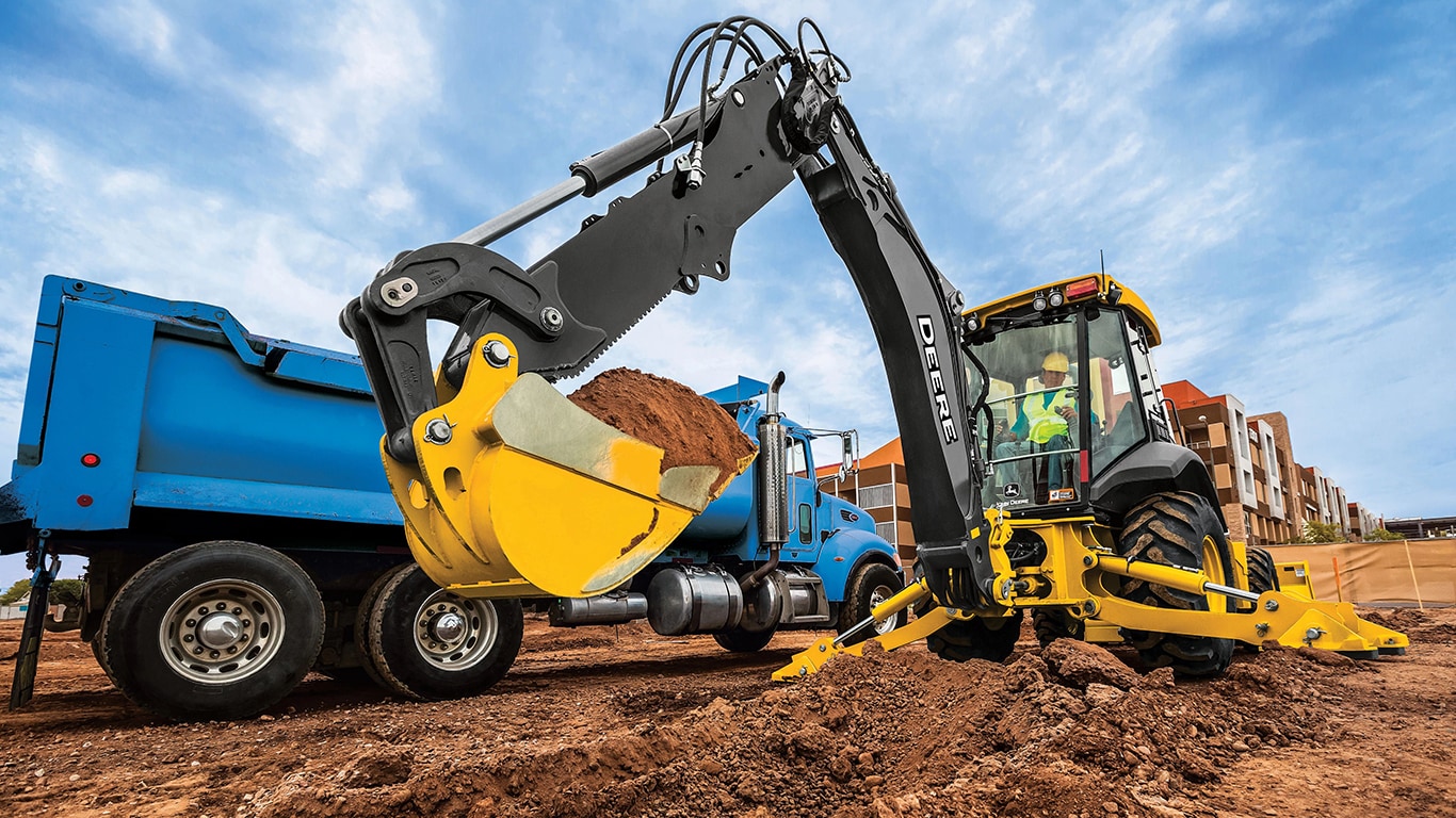 A 410P Backhoe loading dirt into a blue dump truck.