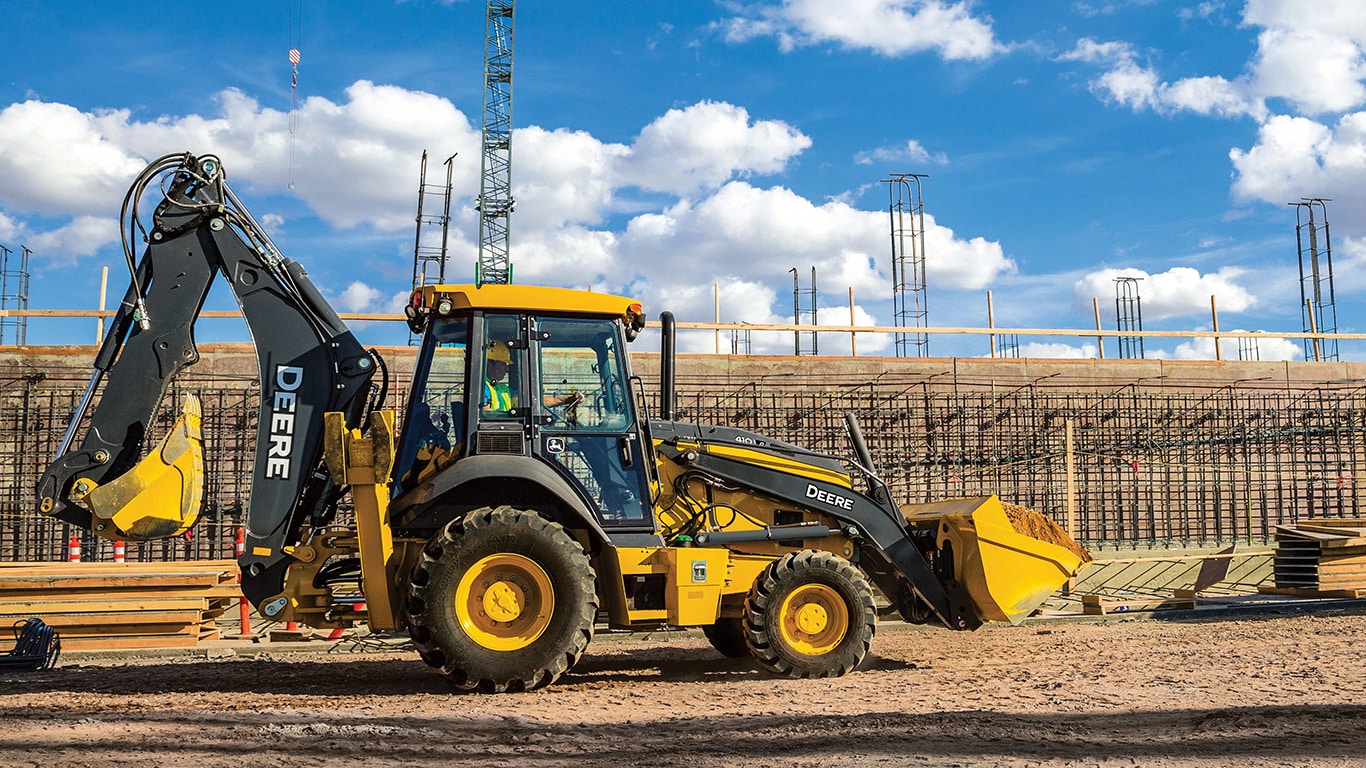 Une pelle-rétro 410P avec des matériaux de construction et des grues en arrière-plan.