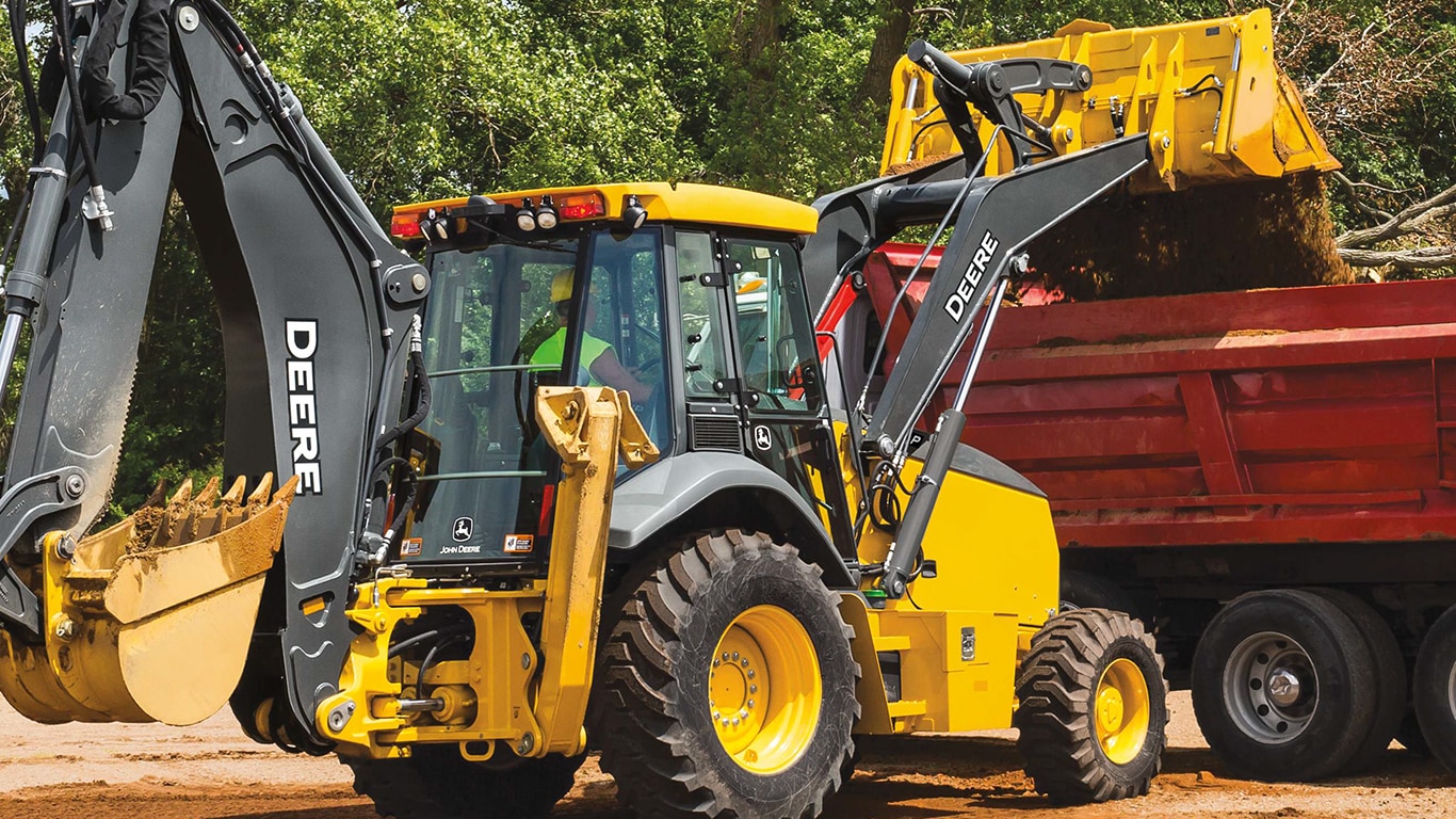 A 710P-Tier Backhoe dumping dirt into a red dump truck.