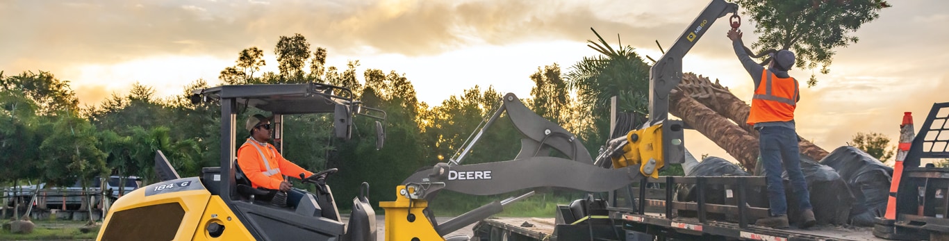 Un employ&eacute; d'une chargeuse &agrave; roues compacte John Deere 184 G-Tier abaisse un accessoire MB60 pour ramasser un palmier.