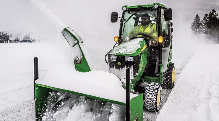 A person using a 1025R Mower with a snow blower attachment to clear snow.