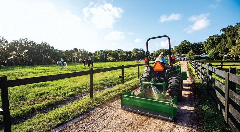 Une personne conduisant son tracteur 3025E sur un chemin de terre