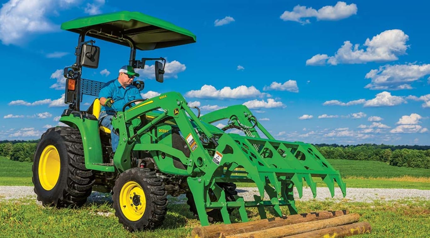 A person using his 3023E Tractor to clear out logs from a field.