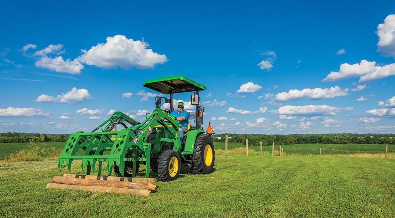 A person picking up logs with his 3032E Tractor.