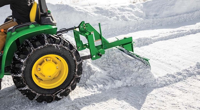 Un tracteur 3032E doté d’un accessoire de déneigement et de chaînes sur ses pneus.