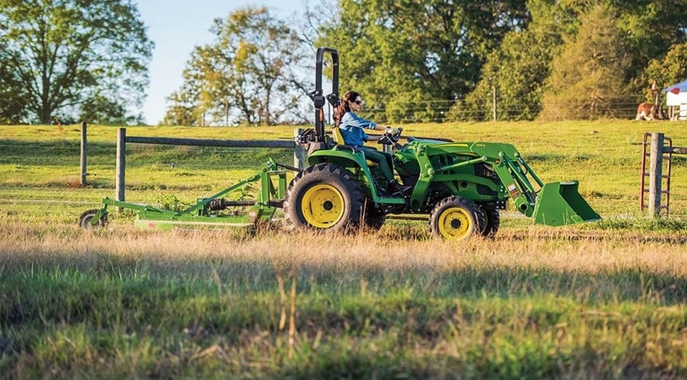 A person driving her 3038E Tractor into a pasture.