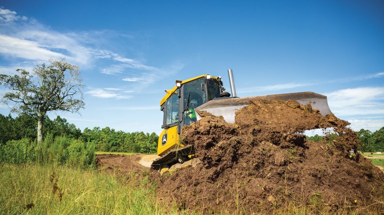 Front view of a 450P Dozer pushing dirt with trees in the background.