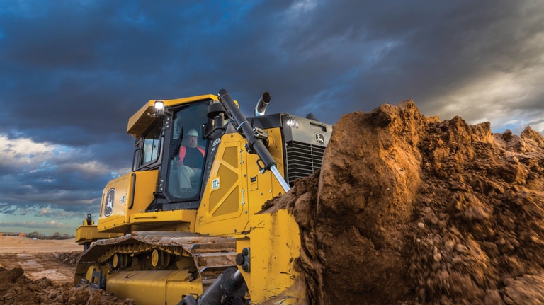 A close-up of an 850L Dozer pushing dirt with a cloudy sky in the background.