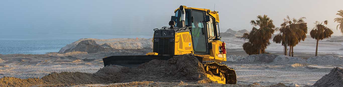 Bouteur chenillé John Deere déplaçant des tas de matériaux organiques.