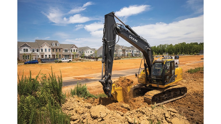 A 160P-Tier Excavator moving dirt at a worksite with a housing development in the background.