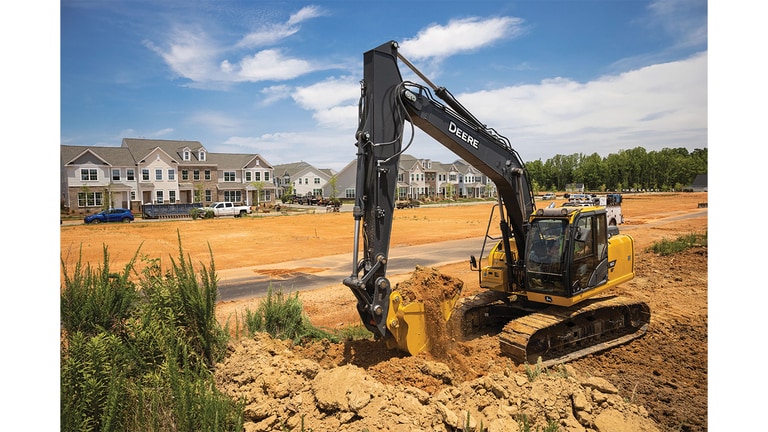 Excavatrice 160P-Tier déplaçant de la terre sur un chantier avec un lotissement en arrière-plan.