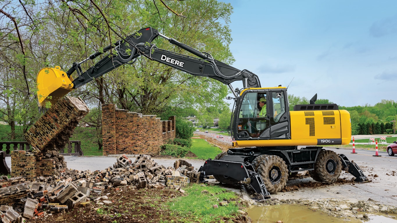 Une excavatrice 190GW utilisée pour briser un mur de briques devant une route.