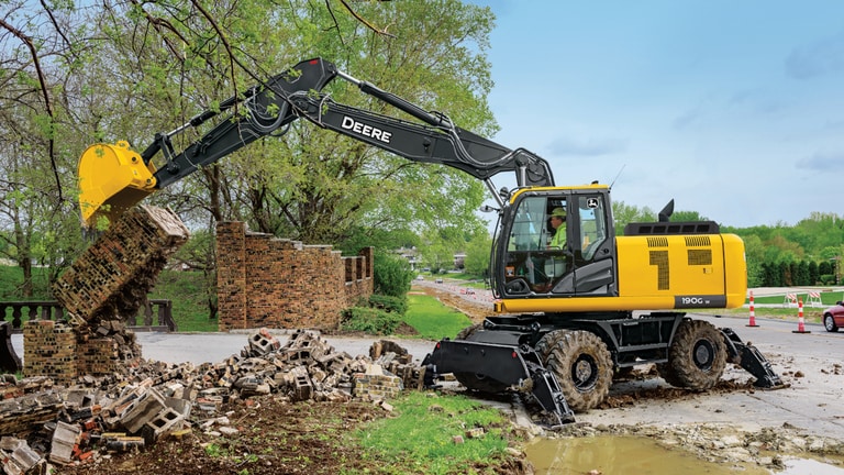 Une excavatrice 190GW utilisée pour briser un mur de briques devant une route.