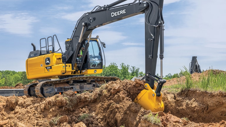 Une excavatrice 200G ramassant de la terre et de l’herbe sur un chantier.