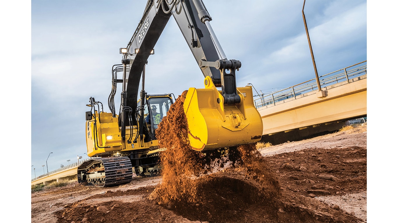 Un opérateur qui utilise une excavatrice 245P-Tier pour ramasser de la terre sur un chantier avec un viaduct en arrière-plan.