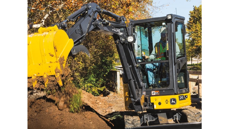 Un opérateur utilisant une excavatrice 26P pour déverser de la terre sur une pile devant une clôture.