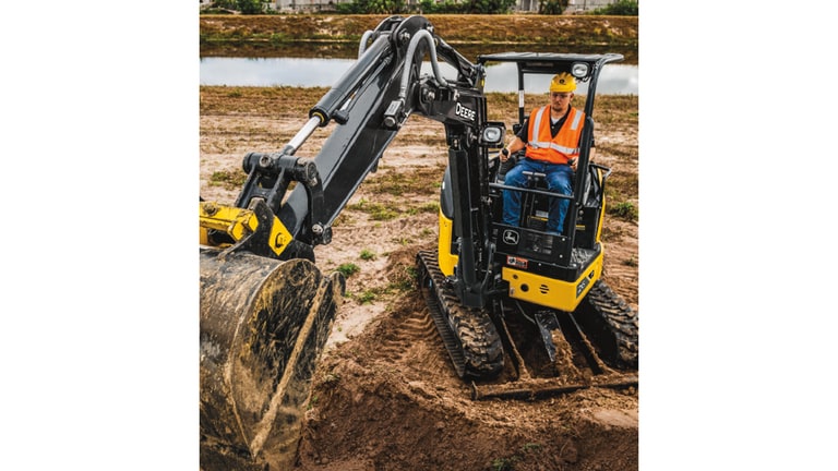 Un opérateur qui utilise une excavatrice 26P pour ramasser de la terre sur un chantier avec un étang en arrière-plan.