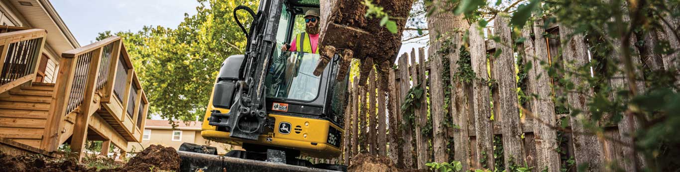 35G Mini Excavator digging dirt between a fence and a deck in a residential landscaping project