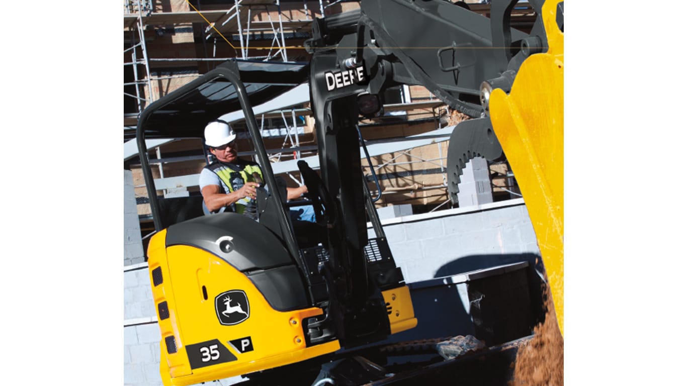 A close-up of an operator using a 35P-Tier Excavator to move dirt at a worksite with building construction in the background.