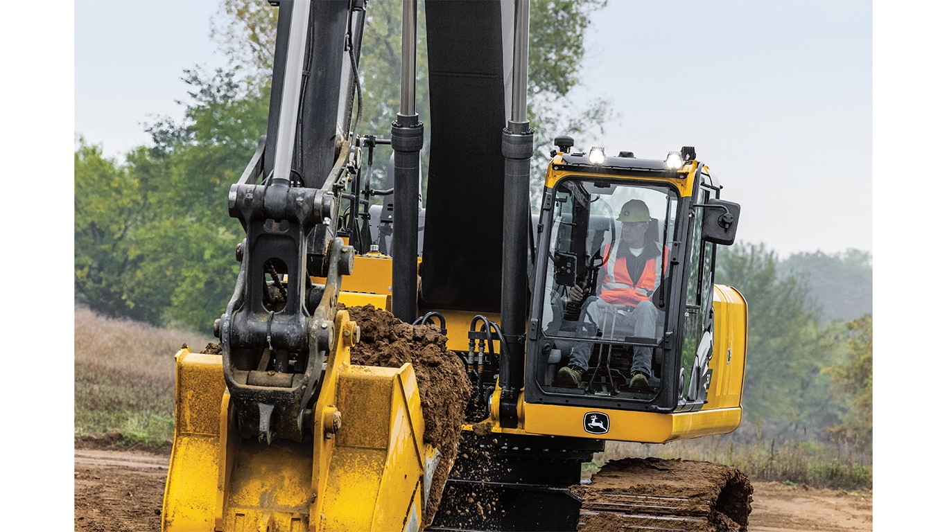 Un opérateur qui utilise une excavatrice 380P-Tier pour déplacer de la terre sur un chantier avec des arbres en arrière-plan.