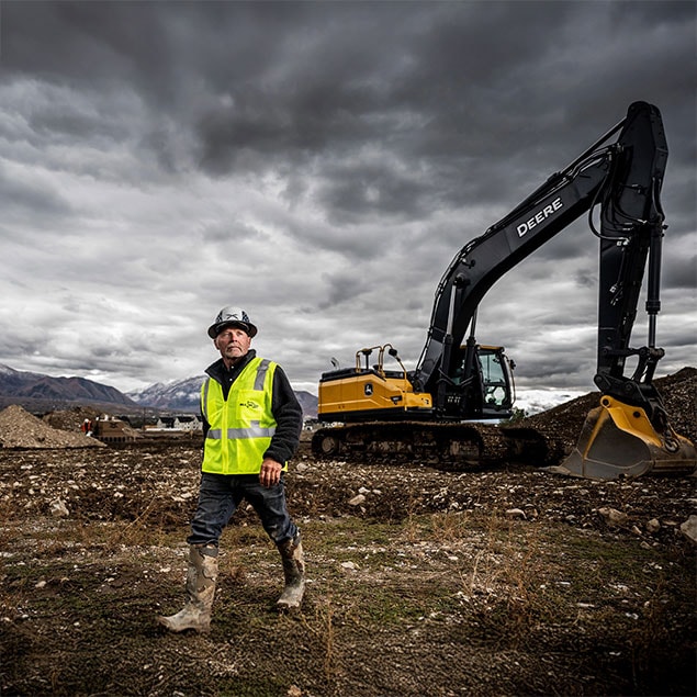 person waking under a cloudy day next to deere excavator on a field