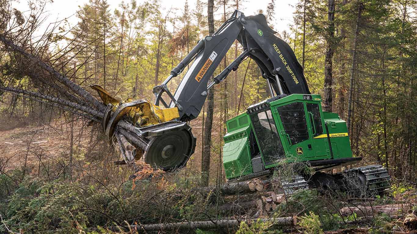 Abatteuse-groupeuse chenill&eacute;e verte qui coupe et saisit des arbres dans une clairi&egrave;re au milieu d'une for&ecirc;t dense.