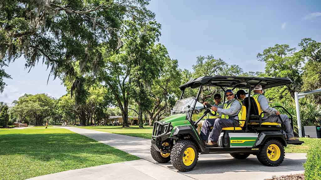 Un véhicule Gator vert transportant quatre passagers portant des vestes de travail circule sur la chaussée​