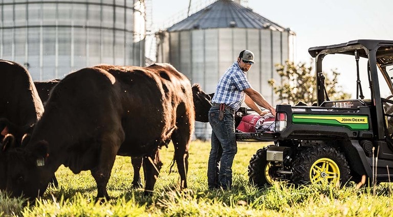 A person unloading feed from a XUV835M Gator for his cattle.