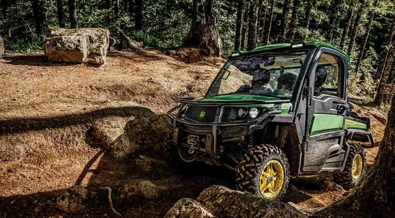 Un tracteur Gator XUV835M circulant hors route sur des rochers dans une forêt dense