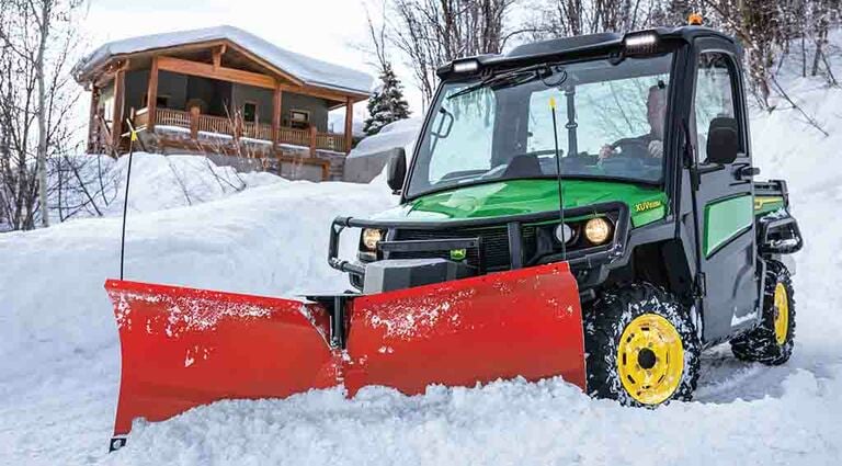 a XUV835M Gator with a snowplow attachment in front of a snowy cabin