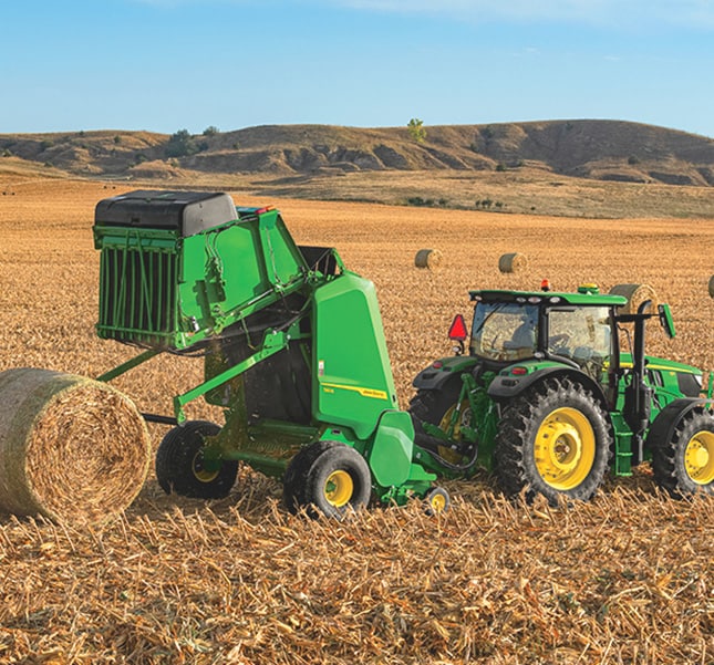 Tracteur tirant une presse dans un champ de foin avec une balle ronde éjectée.
