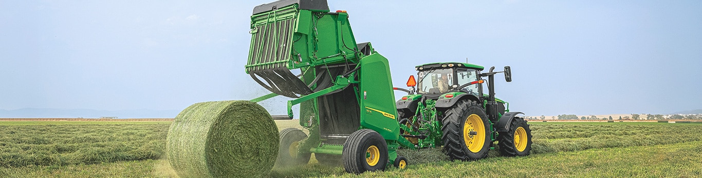 Tracteur et presse éjectant une balle de foin dans un champ.