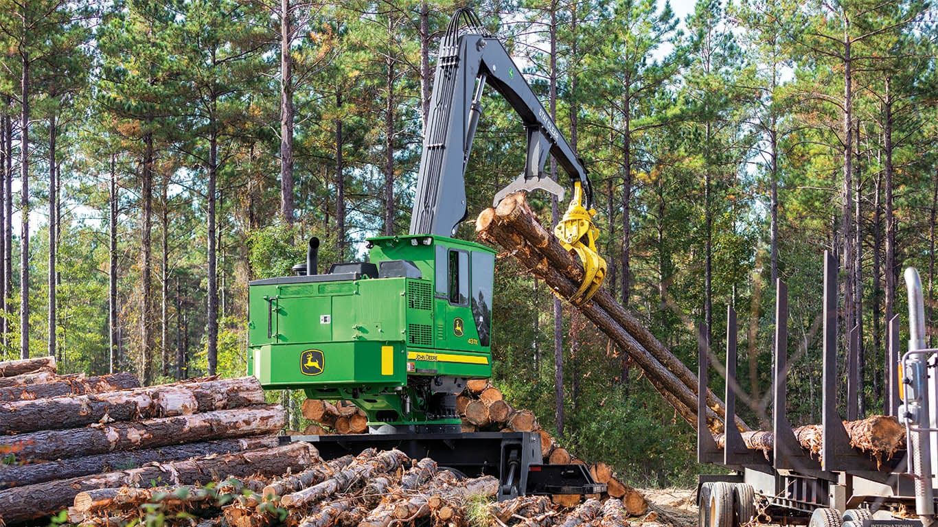 Une grue de chargement John&nbsp;Deere se prépare à ajouter des rondins dans la plate-forme d'un camion forestier.