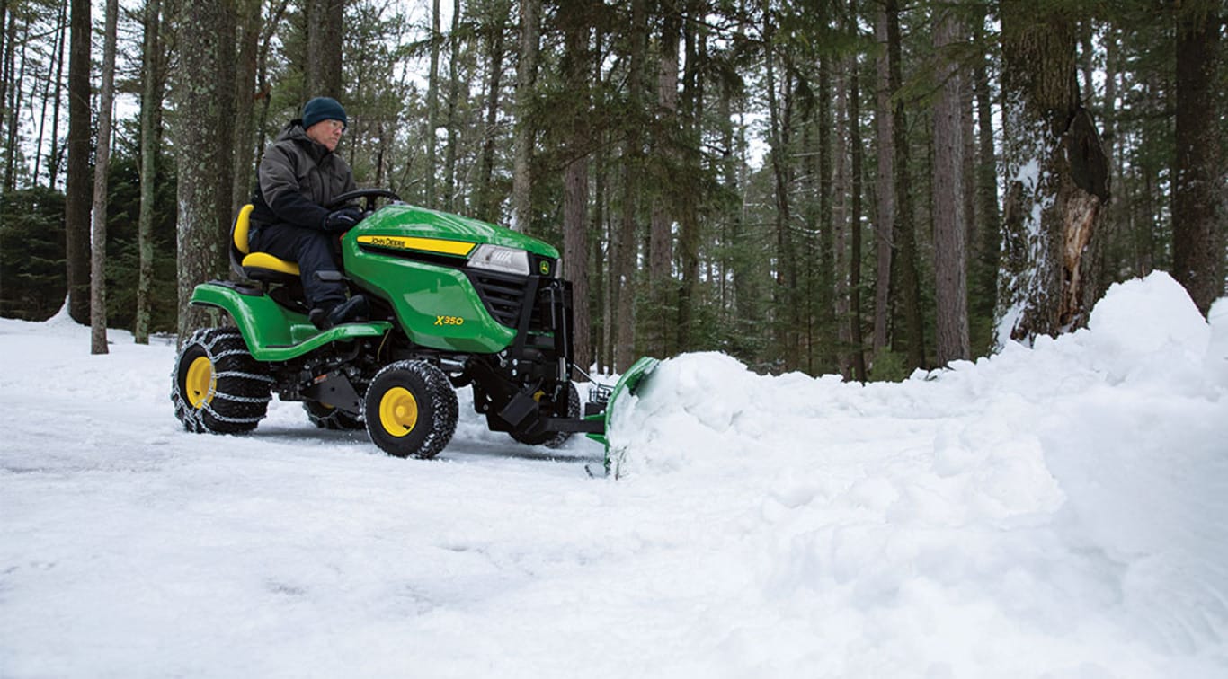 Une personne déneige le sol avec son tracteur X350 doté d’une souffleuse