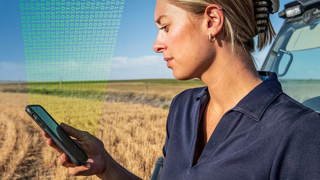 Female farmer in a field, viewing John Deere Operations Center™ on her mobile phone.