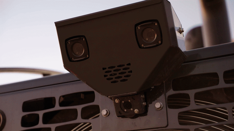 Close-up of a black, box-shaped camera with two lenses and ventilation holes mounted on a structure.