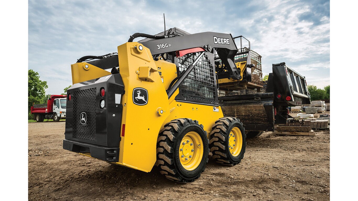 A 316G Skid Steer with pallet attachment loads a pallet of rocks onto a truck.