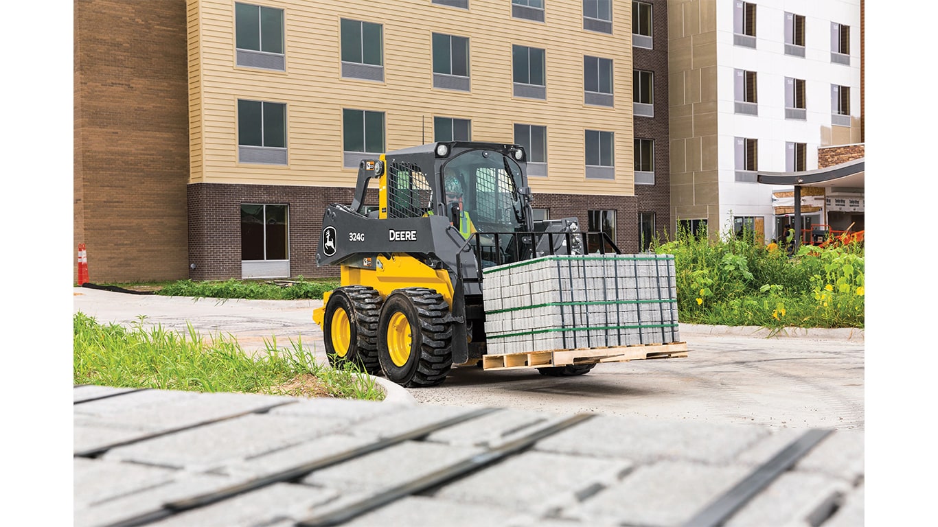 Une chargeuse à direction différentielle 324G équipée d’une fourche à palette transportant des briques devant un chantier.