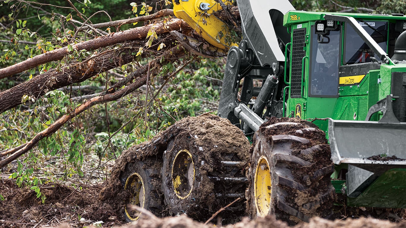 768L-II skidder moving a pile of trees on a muddy work site.
