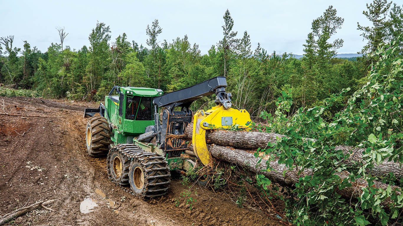 A John Deere skidder lifting logs in a forest