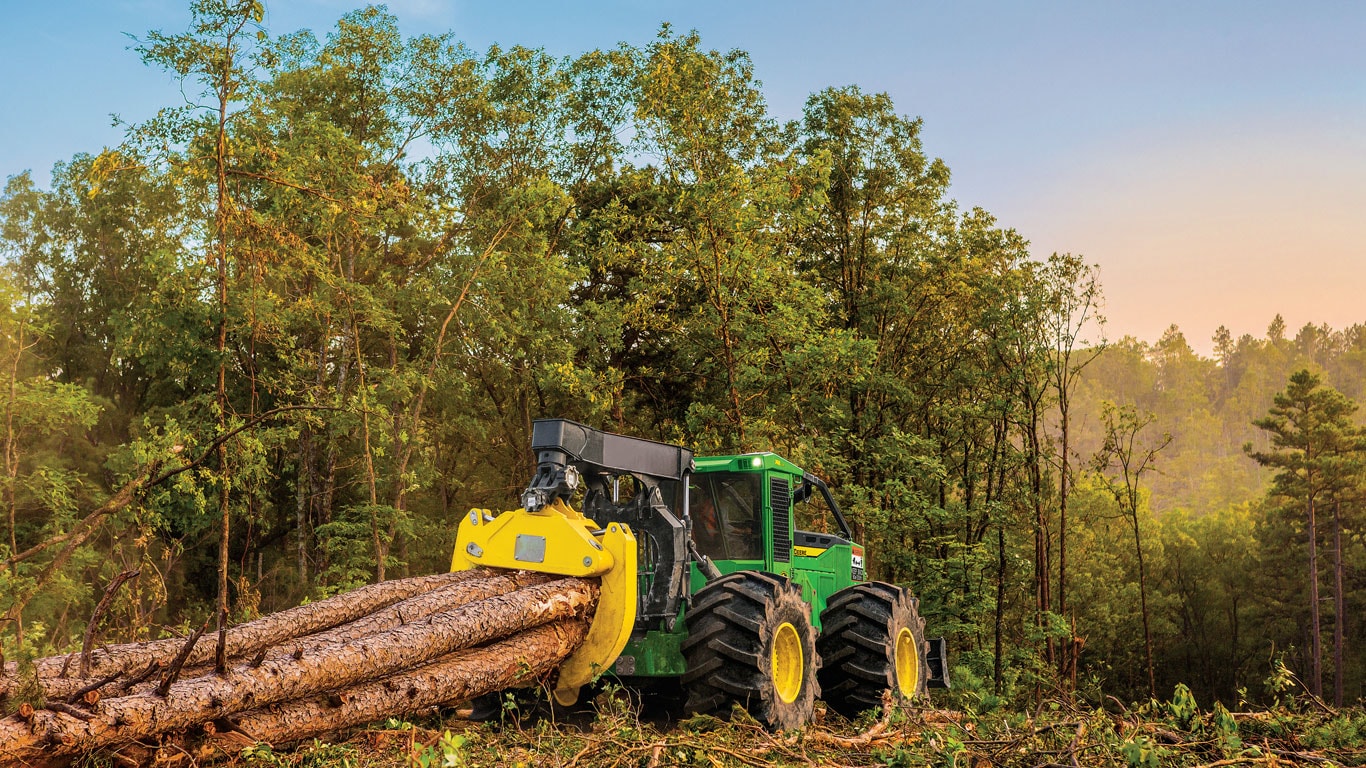 John Deere 748L Skidder moving cut logs through a clearing.