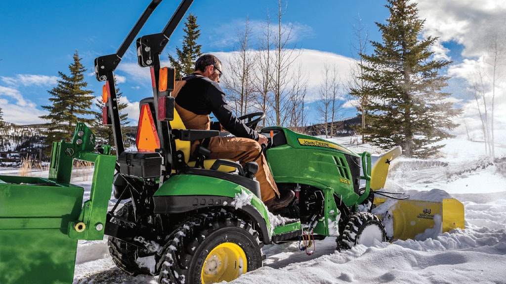 Un homme conduit un tracteur compact 1025R soufflant de la neige avec une souffleuse à neige de 54