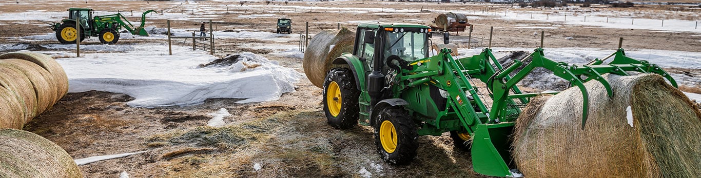 Tracteurs 6M avec pince et balle ronde dans un ranch pour bétail en hiver avec les montagnes en arrière-plan
