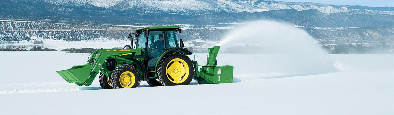 Tracteur 5M avec chargeur et chasse-neige soufflant la neige en hiver