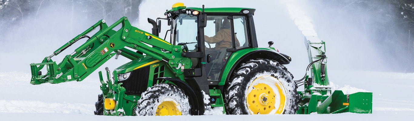 Tracteur de la série 6M avec chargeur et chasse-neige soufflant la neige en hiver