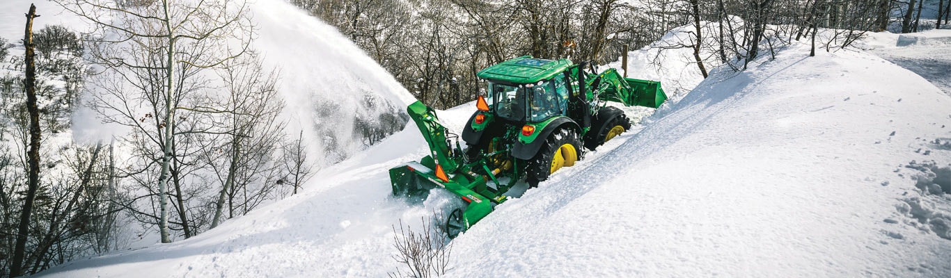 Tracteur 5M avec chargeur et chasse-neige sur les pentes, soufflant la neige en hiver