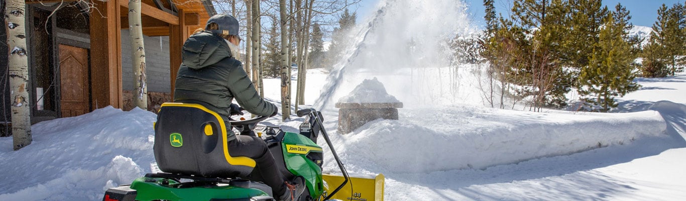 Une femme qui conduit un tracteur de pelouse série 100 chasse la neige avec un chasse-neige