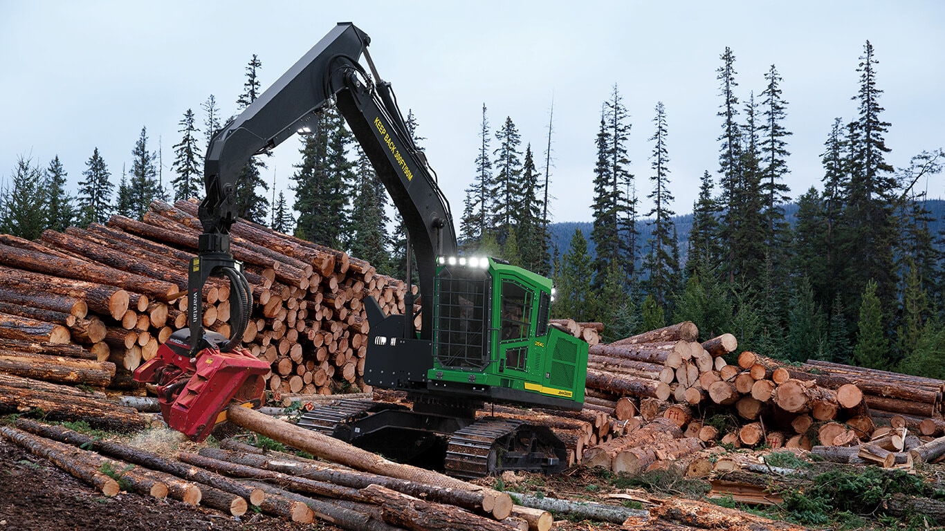 A John&nbsp;Deere swing machine dropping logs onto a pile with trees in the background.