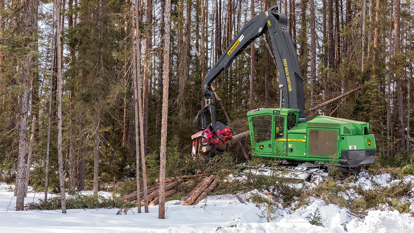 Une abatteuse-façonneuse chenillée de John Deere qui coupe des rondins à longueur dans une forêt enneigée.