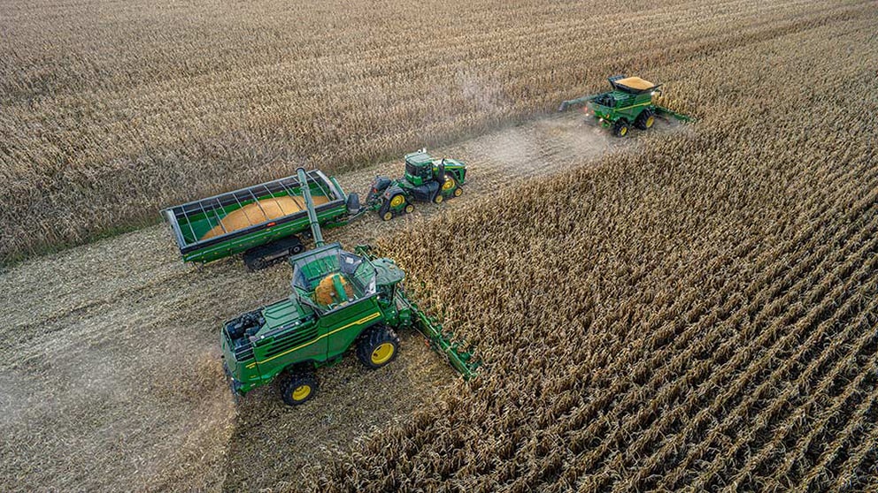 Combines and tractors pulling a grain cart in field